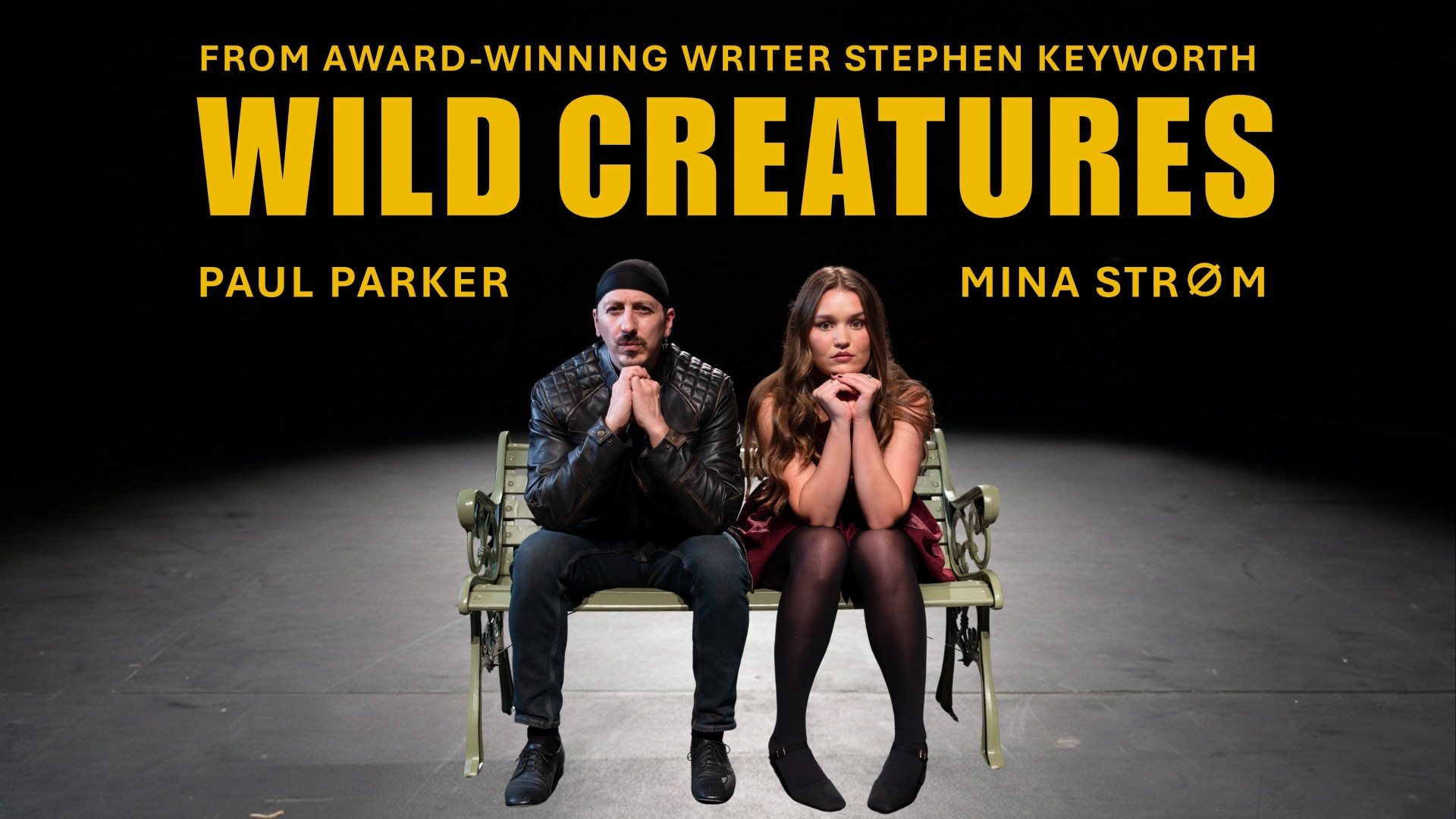 Wild Creatures, a man and a woman sit on a bench looking at the camera